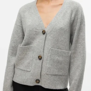 Grå kofta från Vero Moda - Mysig grå kofta från Vero moda med v-ringning och tre knappar framtill. Koftan har två stora fickor och ribbade muddar vid ärmslut och nederkant. Perfekt att slänga över en t-shirt för en chill look.