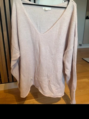 Ljusrosa stickad tröja från H&M - Mysig ljusrosa stickad tröja från H&M med djup V-ringning och avslappnad passform. Tröjan har långa ärmar och är tillverkad i ett mjukt material som känns skönt mot huden. Perfekt för lager-på-lager och chill dagar.