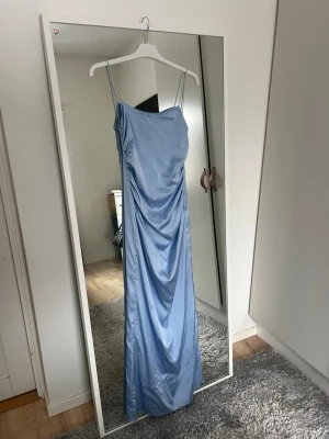Ljusblå långklänning - Ljusblå balklänning med tunna axelband och draperad framsida. Klänningen har en slit på vänster benet som inte finns på nellys original klänning då vi lämnade in den till en skräddare, använd 1 gång💗Original pris: 899kr 