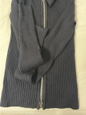 Svart ribbad ziptröja med krage - Säljer en svart ribbad tröja med dragkedja framtill och hög krage. Tröjan har långa ärmar och är gjord i ett stretchigt material som sitter snyggt. Enkel och clean design som funkar till det mesta.