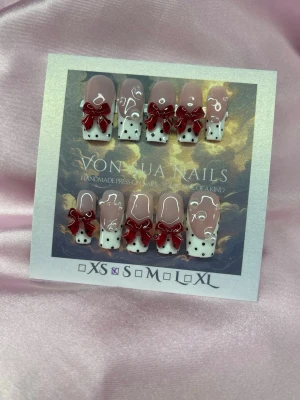 CherryNoir (S);Medium Square - Handgjorda press-on naglar i nude och vitt med svarta prickar, dekorerade med 3D-röda rosetter och vita pärlor. Naglarna har en medium squareform. Passar dig  som vill ha något unikt och trendigt på naglarna.S: 15 mm, 11,5 mm, 12 mm, 11 mm, 9 mm 