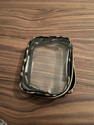 Transparent sminkväska med leopardmönster - Praktisk sminkväska med transparent plast på båda sidor och leopardmönstrad kant. Väskan har dragkedja runt om och är perfekt för att organisera smink eller skönhetsprodukter. Enkel att se innehållet tack vare det genomskinliga materialet.