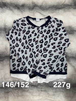 Grå leopardmönstrad tröja - Säljer en grå långärmad tröja med leopardmönster. Tröjan har ribbade muddar vid hals, ärmslut och nederkant samt en vit detalj nedtill som ger en lager-på-lager-look. Perfekt för dig som gillar djurmönster och vill sticka ut.🌸 Fint använt skick. Storlek 146/152 