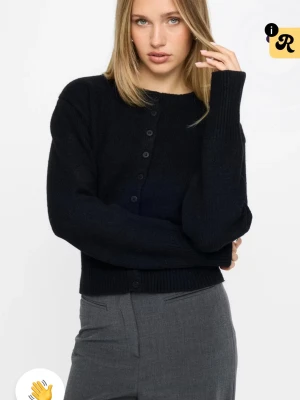 Svart figursydd stickad kofta med knappar från Bikbok - Mysig svart stickad kofta med rund halsringning och knäppning framtill. Koftan har långa ärmar och ribbade muddar vid ärmslut och nederkant. Perfekt att slänga över en t-shirt eller topp för en enkel och stilren look.