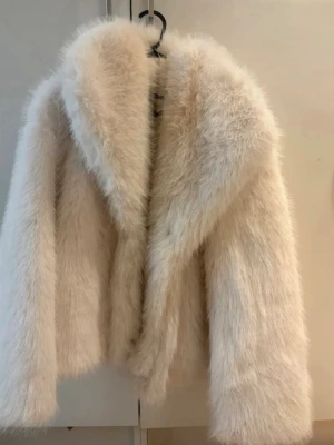 Vit fluffig fuskpälsjacka  - Supersnygg vit fuskpälsjacka från med bred krage och lång ärm. Jackan har en riktigt fluffig och mjuk känsla, perfekt för att hålla värmen under kalla dagar. Enkel att matcha och ger en lyxig vibe till din outfit.