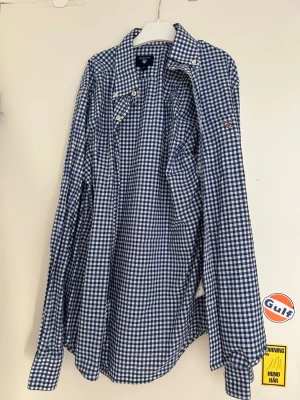 Blårutig skjorta från Gant - Klassisk blårutig skjorta från Gant i bomull. Skjortan har lång ärm, vit-blå rutigt mönster och knappar framtill. Perfekt för en stilren och avslappnad look. Gant-logga på bröstet och snygg krage.