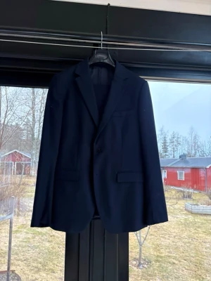 Mörkblå klassisk kostym - Snygg mörkblå kavaj med enkelknäppning och klassiska slag. Två fickor med lock framtill och en bröstficka. Perfekt till kostym eller att styla med jeans för en mer avslappnad look.