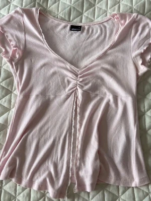 Ljusrosa topp - Supersöt ljusrosa topp från ginatricot. V-ringad med korta ärmar och volangkant. Tunn och mjuk i bomullsmix, perfekt för vår och sommar. Storlek S men passar även mig som har storlek XS eller 158/164. Pris går att diskutera🥰