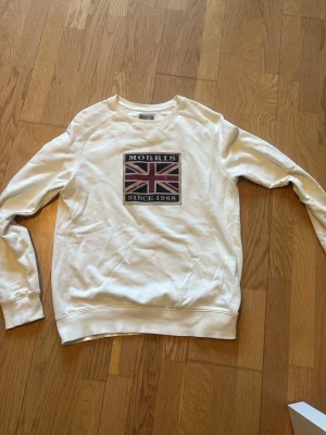 Vit sweatshirt från Morris S - Vit sweatshirt från Morris med tryck av brittiska flaggan och texten 'Morris Since 1968' på bröstet. Tröjan har rund hals, långa ärmar och ribbade muddar. Perfekt för en avslappnad och stilren look.
