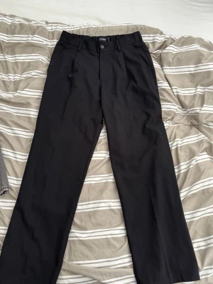 Svarta kostymbyxor med rak passform - Snygga svarta kostymbyxor med rak passform. Byxorna har resår baktill i midjan, knapp och dragkedja framtill samt diskreta fickor. Perfekta för en clean och stilren look.