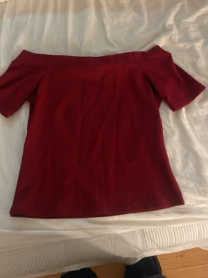 Mörkröd offshoulder topp - Trendig mörkröd offshoulder topp med korta ärmar. Snygg och enkel design som passar perfekt till jeans eller kjol. Materialet känns mjukt och stretchigt, vilket gör toppen bekväm att bära. Perfekt för dig som vill ha en stilren och modern look.