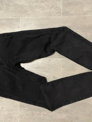 Svarta raka jeans för barn stl 150 - Säljer ett par svarta jeans med rak passform och klassisk femficksdesign. Jeansen har en enkel look utan synliga slitningar eller dekorationer, perfekta för en clean och stilren outfit. Materialet känns som bomullsdenim.