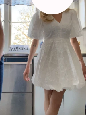 Vit kort klänning med puffärmar - De är tunna broderade blommor på klänningen och klänningen har inte använts så mycket! Köptes för 899kr