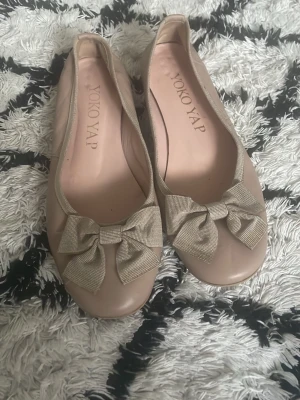 Rosa ballerinaskor med rosett - Snygga rosa  ballerinaskor från Yoko Yap med rund tå och dekorativa rosetter framtill. Skorna har en glansig finish och är tillverkade i ett slätt material som ger en stilren look. Perfekta för dig som gillar klassisk och söt stil.