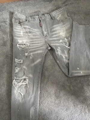 Grå slitna jeans från Dsquared2 - Säljer ett par grå jeans från Dsquared2 med distressed detaljer, slitningar och färgstänk. Mycket bra skick. perfekt för sommar och vinter.  Pris kan diskuteras!