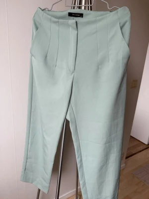 Mintgröna kostymbyxor från N-Value - Snygga mintgröna kostymbyxor  med hög midja och pressveck framtill. Byxorna har raka ben och diskreta fickor i sidorna. Perfekta för en clean och stilren look. Materialet känns mjukt och har en lätt stretch.