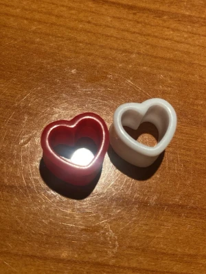 Hjärtpluggar i plast, röd & vit - Två coola hjärtformade pluggar i plast, en röd och en vit. Perfekta som statement-accessoar till öronen för dig som är cool och diameter är 13mm. Säljes för 40kr