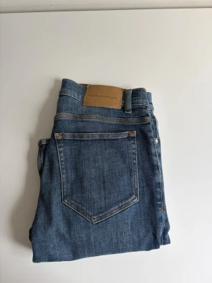 Blå jeans Tiger of Sweden - Säljer ett par klassiska blå jeans från Tiger of Sweden. Jeansen har en smal passform, fem fickor och normal midja. Tillverkade i ett mjukt denimtyg med snygga kontrastsömmar och läderpatch bak i midjan. Storlek, 30/32
