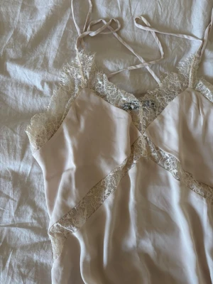 Beige linne  med spetsdetaljer - Säljer ett elegant beige linne med tunna axelband och vackra spetsdetaljer längs kanterna och bysten. Materialet känns mjukt och följsamt, perfekt för mysiga kvällar hemma.