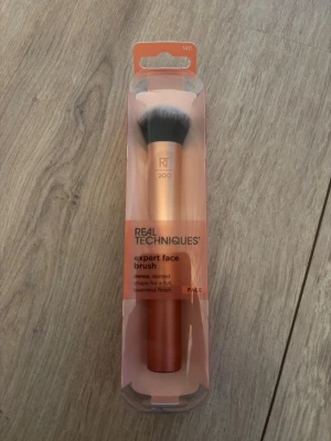 Real Techniques Expert Face Brush - Expert Face Brush från Real Techniques med täta, kupolformade borst. Handtaget är i metallic orange och borsten är svart med vita toppar. Perfekt för flytande och krämiga foundations. Vegansk och cruelty-free borste som ger ett sömlöst resultat.