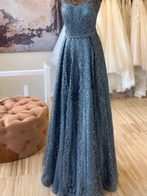 Glittrig blå långklänning - Helt ny, elegant blå långklänning med glittrigt mönster och markerad midja. Klänningen har en v-ringad överdel och är ärmlös, vilket ger en stilren och festlig look. Perfekt för bal eller festliga tillfällen.