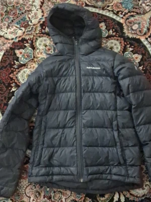 Svart pufferjacka Peak Performance S - Säljer en svart pufferjacka från Peak Performance med huva och dragkedja framtill. Jackan har quiltad design och är perfekt för kalla vinterdagar. Lätt och smidig att bära, med diskret logga på bröstet. Passar dig som vill ha både stil och funktion.