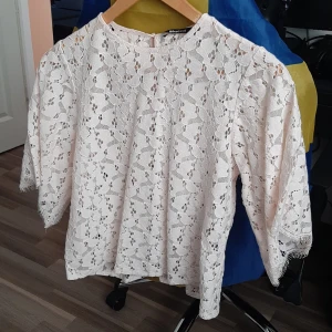 Beige spetsblus från Gina Tricot - Superfin beige blus från Gina Tricot i spets med blommigt mönster. Blusen har trekvartsärmar med fransig kant och rund halsringning. Perfekt för dig som gillar romantisk och söt stil!