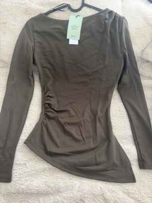 Olivgrön långärmad topp(ordinarie pris 300kr) - Snygg olivgrön långärmad topp med figurnära passform och asymmetrisk nederkant. Tillverkad i mjukt material som känns skönt mot huden. Perfekt att styla med jeans eller kjol för en trendig look.