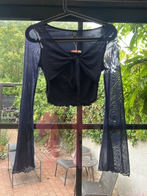 Marinblå mesh  topp med knytning - Trendig marinblå topp med långa, utsvängda ärmar och knytning framtill. perfekt för en cool och edgy look. Tillverkad i ett lätt och stretchigt meshmaterial.