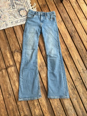 Blå bootcut jeans  - Ett par ljusblå bootcut jeans  klassiska fyra fickor. Jeansen har hög midja och vida ben från knät och ner. Perfekta för en avslappnad och trendig look.
