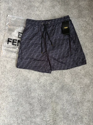 FendiByxor - Snygga svarta byxor med heltryckt FF-monogram i mörkgrått. Klassisk modell med dragsko i midjan och sidofickor. Perfekta för stranden eller poolen, med exklusiv känsla och trendig design.