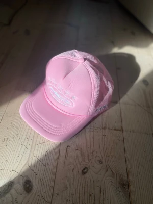 Rosa Cortiez keps - Snygg rosa Cortiez med böjd skärm och mesh på sidorna och bak för extra ventilation. Framtill finns broderade vita detaljer och stjärnor som ger kepsen en trendig vibe. Perfekt accessoar för att lyfta din streetwear-look.