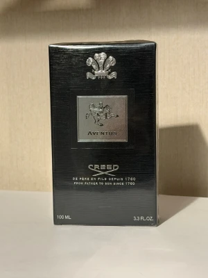 Creed Aventus Eau de Parfum 100 ml - Creed Aventus Eau de Parfum i 100 ml flaska. Lyxig parfym i svart och silver förpackning med elegant logotyp och detaljer. Doften är känd för sin fräscha, fruktiga och maskulina karaktär. Perfekt för dig som vill sticka ut med en exklusiv signaturdoft.