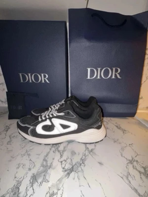 Sneakers med vit logga - Snygga svarta sneakers från B30 med vit CD-logga på sidorna och vita detaljer. Skorna har en chunky vit sula, svarta meshpaneler och vita skosnören. Perfekta för dig som vill sticka ut med exklusiva och trendiga sneakers.