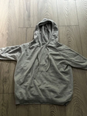 Ljusgrå stickad  hoodie med huva - En enkel och stilren ljusgrå hoodie med huva och dragsnören. Hoodien har långa ärmar, ribbade muddar vid ärmslut och nederkant samt en avslappnad passform. Perfekt för en chill och bekväm look. Materialet känns mjukt och skönt mot huden.