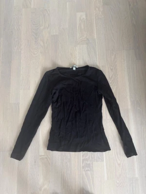 Svart långärmad topp - En enkel svart långärmad topp med rund halsringning. Modellen är figurnära och passar perfekt till lager på lager eller som basplagg. Tillverkad i mjukt material för en bekväm känsla.