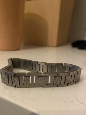 Stilrent armband i rostfritt stål - Snyggt armband i silverfärgat rostfritt stål med rektangulära länkar och detaljerade mönster på vissa länkar. Modern och minimalistisk design som passar till många stilar. Perfekt accessoar för dig som gillar stilrena smycken.