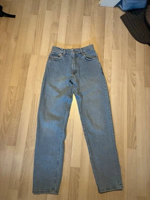 Ljusblå raka jeans - Säljer ett par ljusblå jeans med hög midja och raka ben. Klassisk femficksmodell i denim med knapp och dragkedja framtill. Jeansen har råa kanter nertill för en avslappnad look. 