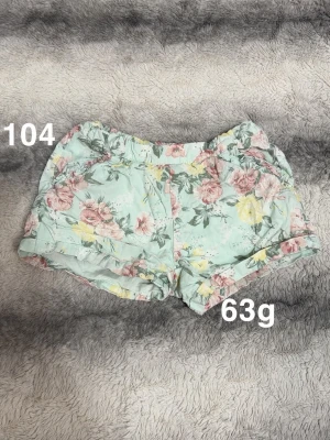 Blommiga mintgröna shorts - Snygga mintgröna shorts med blommigt mönster i rosa och gult. Shorts med elastisk midja och uppvikta benslut, perfekta för varma dagar. Lätta och bekväma, passar dig som gillar en fräsch och somrig stil.🌸 Fint använt skick. Storlek 104