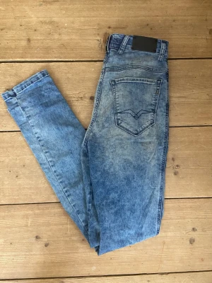 Blå Replay jeans w30  L32 - Säljer ett par blå  Replay jeans med acid wash-effekt och hög midja. Jeansen har klassiska fem fickor och raka ben. Snygga sömmar på bakfickorna ger extra detalj. Perfekta för dig som gillar en retro och avslappnad stil. Har slitning som du kan se på sista bilden.