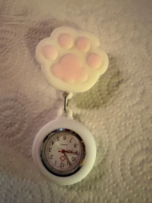 Nurse watch with cat paw design  - This nurse watch features a charming design with a cat paw. The watch is equipped with a quartz movement and has a clear dial with Arabic numerals. It is attached to a retractable clip, making it easy to fasten to work clothes. The back of the watch shows a CE marking.