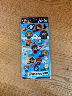 Harry Potter klistermärken - Ett ark med färgglada Harry Potter-klistermärken med motiv av karaktärer som Harry, Ron, Hermione, Hagrid och Dobby samt symboler som glasögon, kvastar och ugglor. Perfekt för att dekorera anteckningsböcker eller datorer.