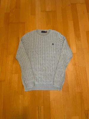 Ljusgrå/blå kabelstickad tröja Polo Ralph Lauren (Large) - 🩵🩶 Ralph Lauren kabelstickad tröja Säljer denna superstilrena, helt oanvänd  kabelstickade tröja från Polo Ralph Lauren i en puderblå färg. Väldigt clean och enkel att styla till både jeans och cargos. Broderad logga på bröstet. ✨ Bra skick ✨ Mjuk och skön passform ✨ Perfekt för höst/vinter ✨Storlek: Large Passar perfekt för en classy/vintage streetwear look!