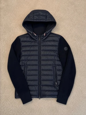 Mörkblå pufferjacka med huva colmar. Nypris 3000kr-zalando - Ny pris är 3000kr. Snygg mörkblå colmar pufferjacka med quiltad framsida och rygg, stickade ärmar och huva. Jackan har dragkedja framtill, två fickor med dragkedja och en diskret logotyp på ärmen. Perfekt för kalla vinterdagar och riktigt skön att bära. Storlek-Herr 174-180cm lång