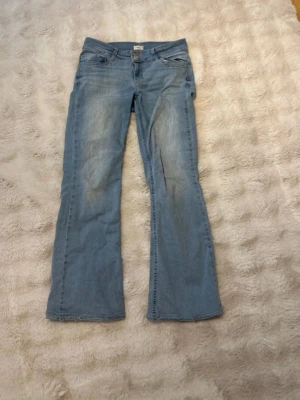 Ljusblå bootcut jeans med brodyr - Säljer ett par ljusblå bootcut jeans med snygg broderad detalj i rosa på bakfickan. Jeansen har klassisk femficksdesign, hällor för skärp och är tillverkade i mjuk denim. Perfekta för dig som gillar en avslappnad och trendig stil. Från nelly, jättesköna och strechiga !❤️