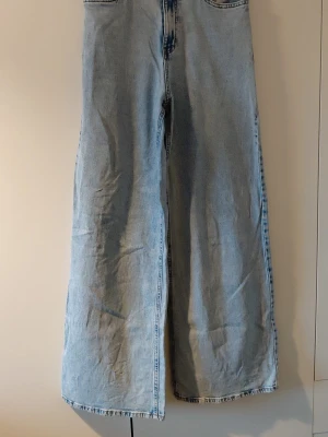 Ljusblå wide leg jeans från Lindex - Säljer ett par ljusblå jeans från Lindex i modellen Viola. Jeansen har hög midja och vida ben för en avslappnad och trendig look. Tillverkade i klassisk denim med snygga sömmar och knappstängning framtill.