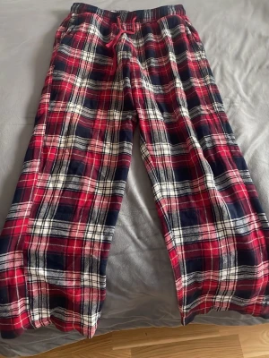 Rutig pyjamasbyxa från Mywear - Pyjamasbyxa från Mywear i storlek S med klassiskt rutigt mönster i rött, blått och vitt. Byxan har resår och snörning i midjan för extra komfort. Perfekt för mysiga kvällar hemma. Den har haft ett hål där nere men det är sytt