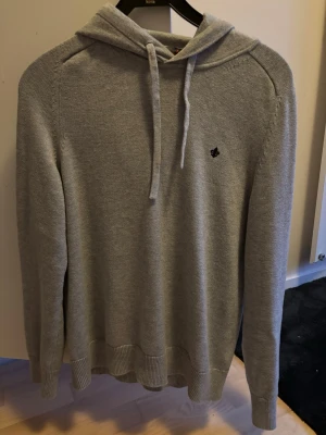 Ny Morris Hoddie  - Snygg ljusgrå stickad hoodie med dragsko i huvan och liten svart brodyr på bröstet. Tröjan har ribbade muddar vid ärmslut och nederkant. Perfekt för en avslappnad och stilren look. Ny pris 1300 mitt pris 699. Har använt hoddien två tre gånger. 