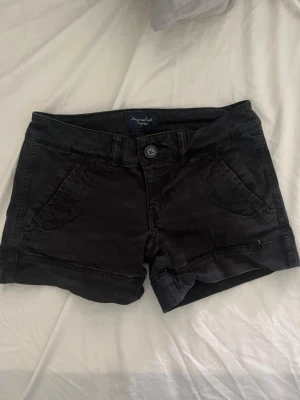 Svarta shorts från American Eagle - Svarta shorts från American Eagle med klassisk femficksdesign och uppvikta benslut. De har knapp- och dragkedjestängning samt två bakfickor. Perfekta för varma dagar och enkla att matcha med allt.