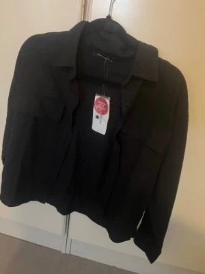 Svart skjorta från Low Classic - Stilren svart skjorta från Low Classic med klassisk krage och två bröstfickor. Skjortan har långa ärmar och en avslappnad passform. Perfekt för dig som gillar minimalistisk och trendig stil.